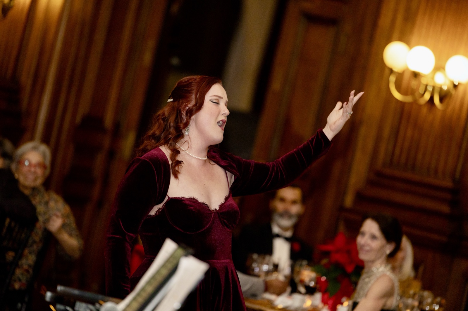 Veronica Richer in a burgundy velvet gown singing at a gala