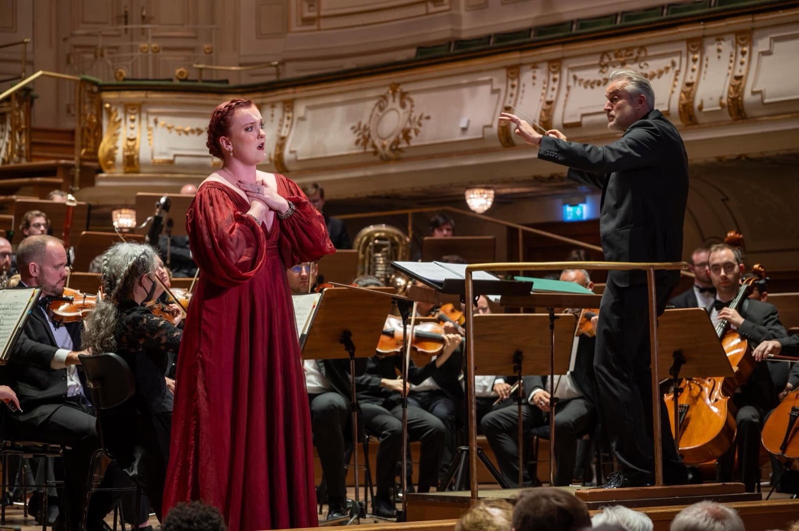 Veronica Richer in a red gown singing with orchestra and conductor