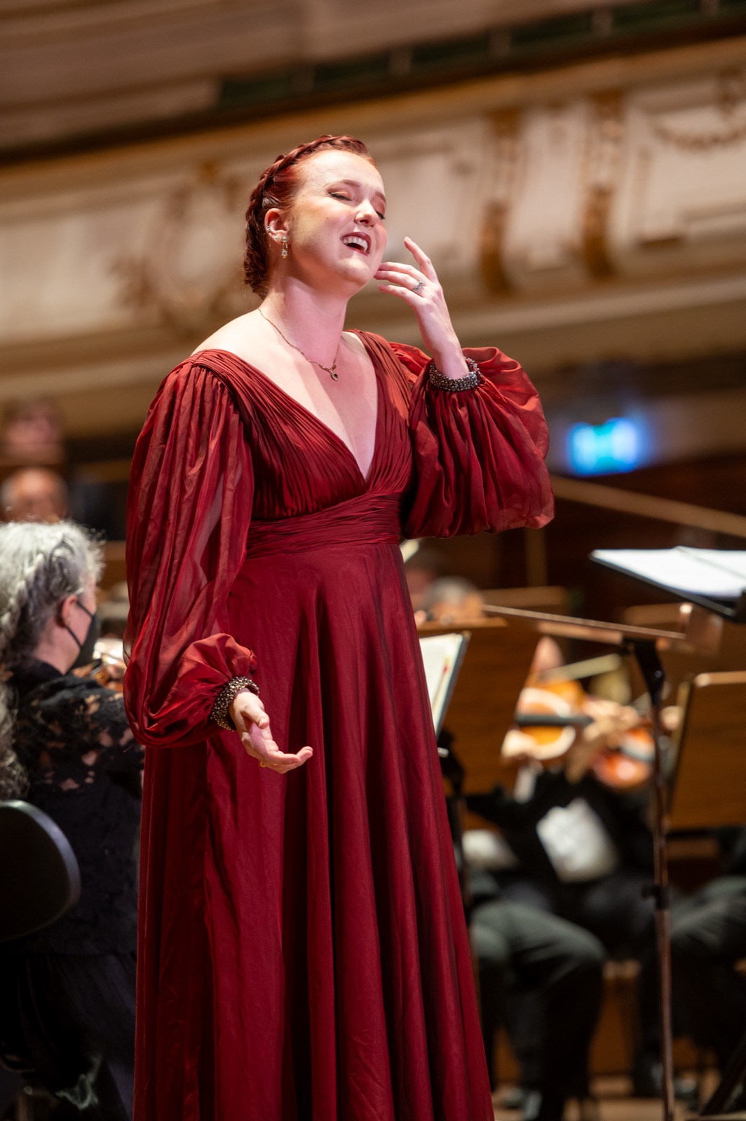 Veronica Richer in a red gown singing with orchestra